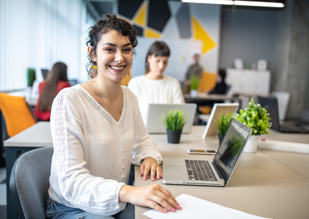 A young lady sitting at a desk with a laptop smiling at the camera