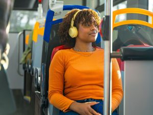 A lady in a bright orange shirt wearing headphones on a public bus