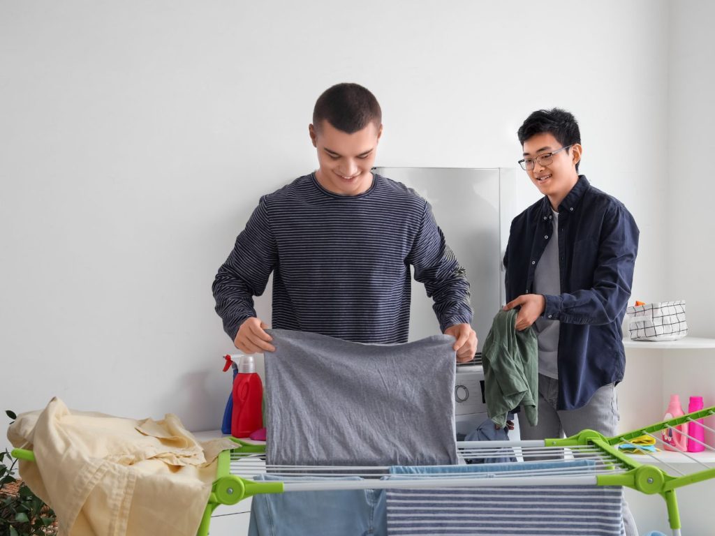 Two young men hanging laundry on an indoor clothes line
