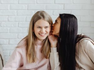A young lady whispering a secret into her friends ear