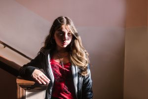 A teenage girl standing in a stairwell looking at the camera tiredly